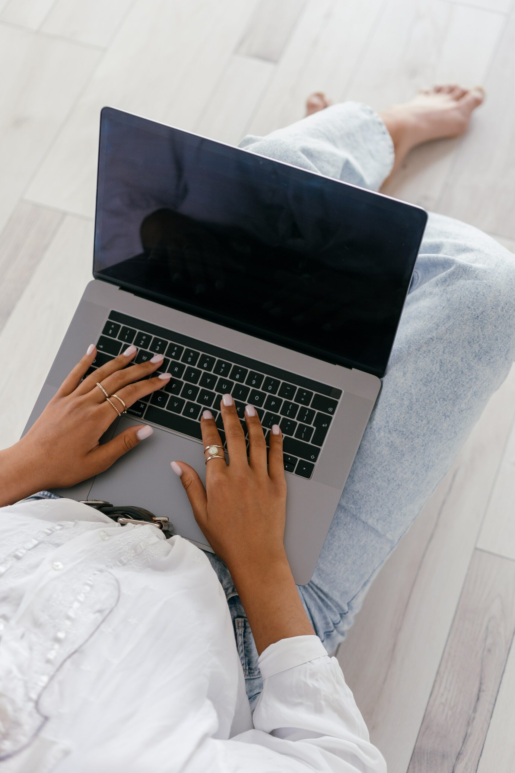 Woman in shirt and jeans sitting on hardwood floor with laptop